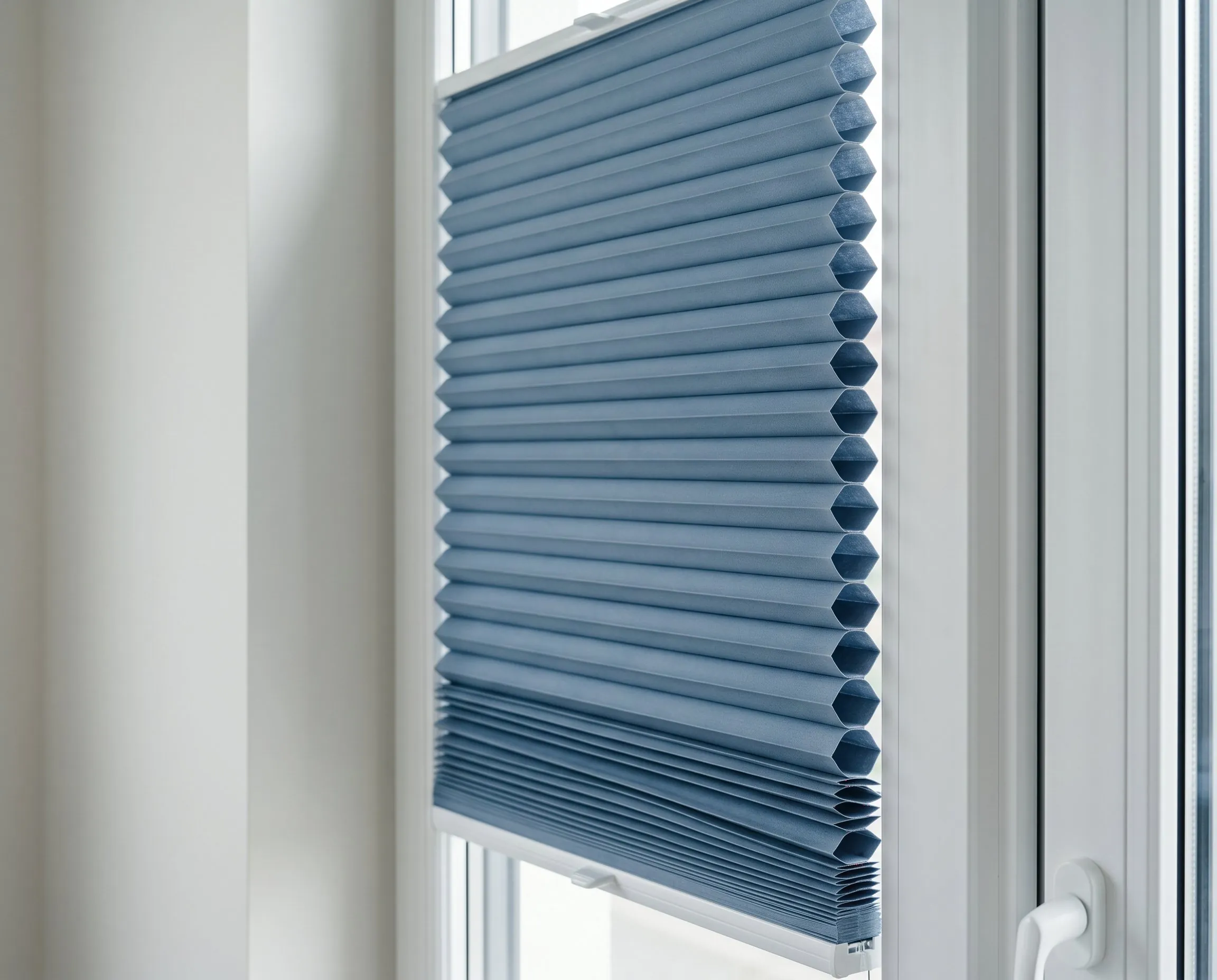 Blaues Wabenplissee halb heruntergelassen vor einem Fenster mit weißem Rahmen.