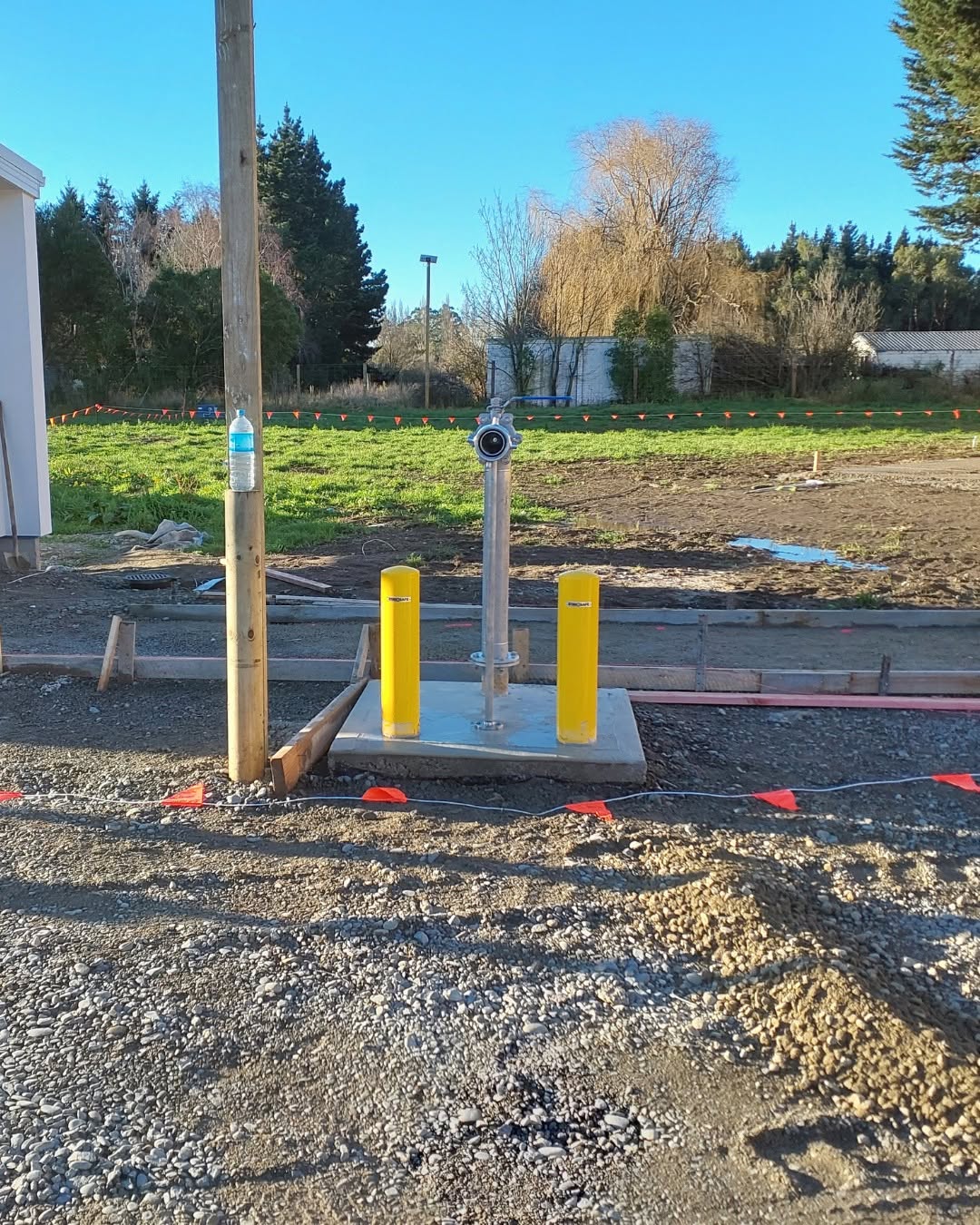 Finished fire hydrant standpipe on a concrete pad between yellow bollards