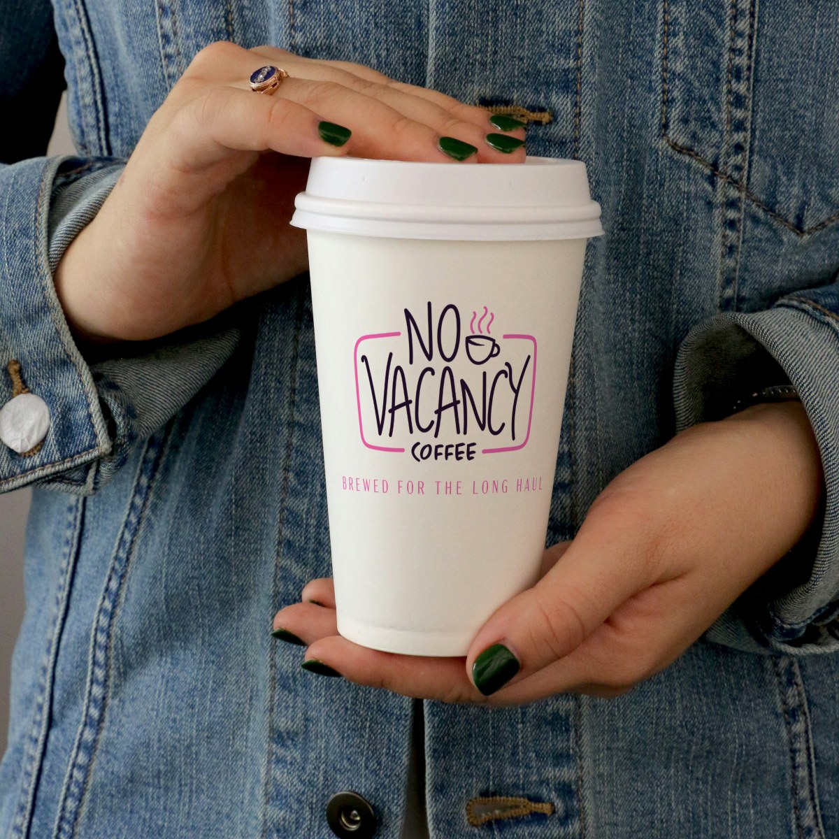 White No Vacancy to-go cup held against a denim jacket