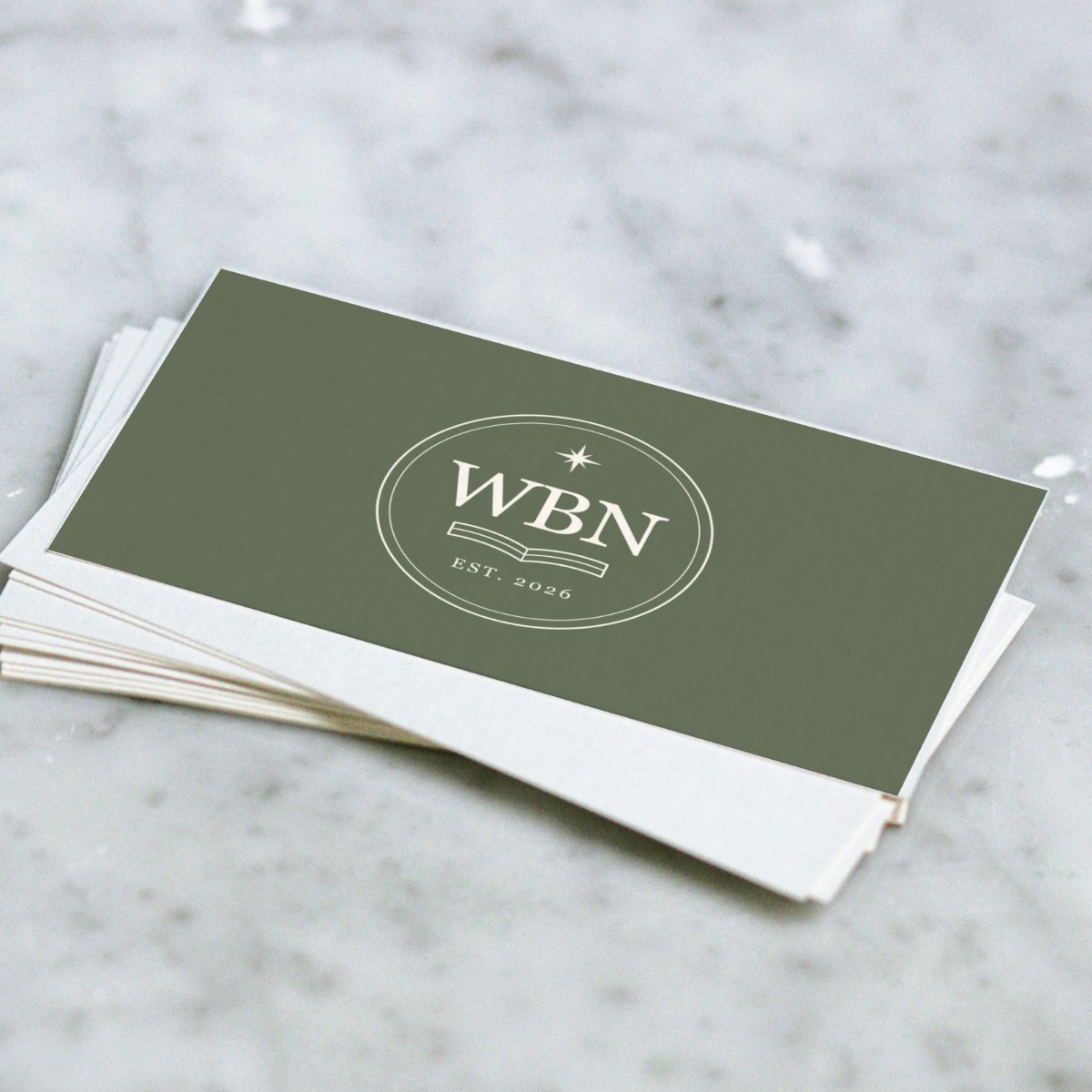 Sage green Wandering Book Nook business cards with the ivory WBN mark, stacked on marble