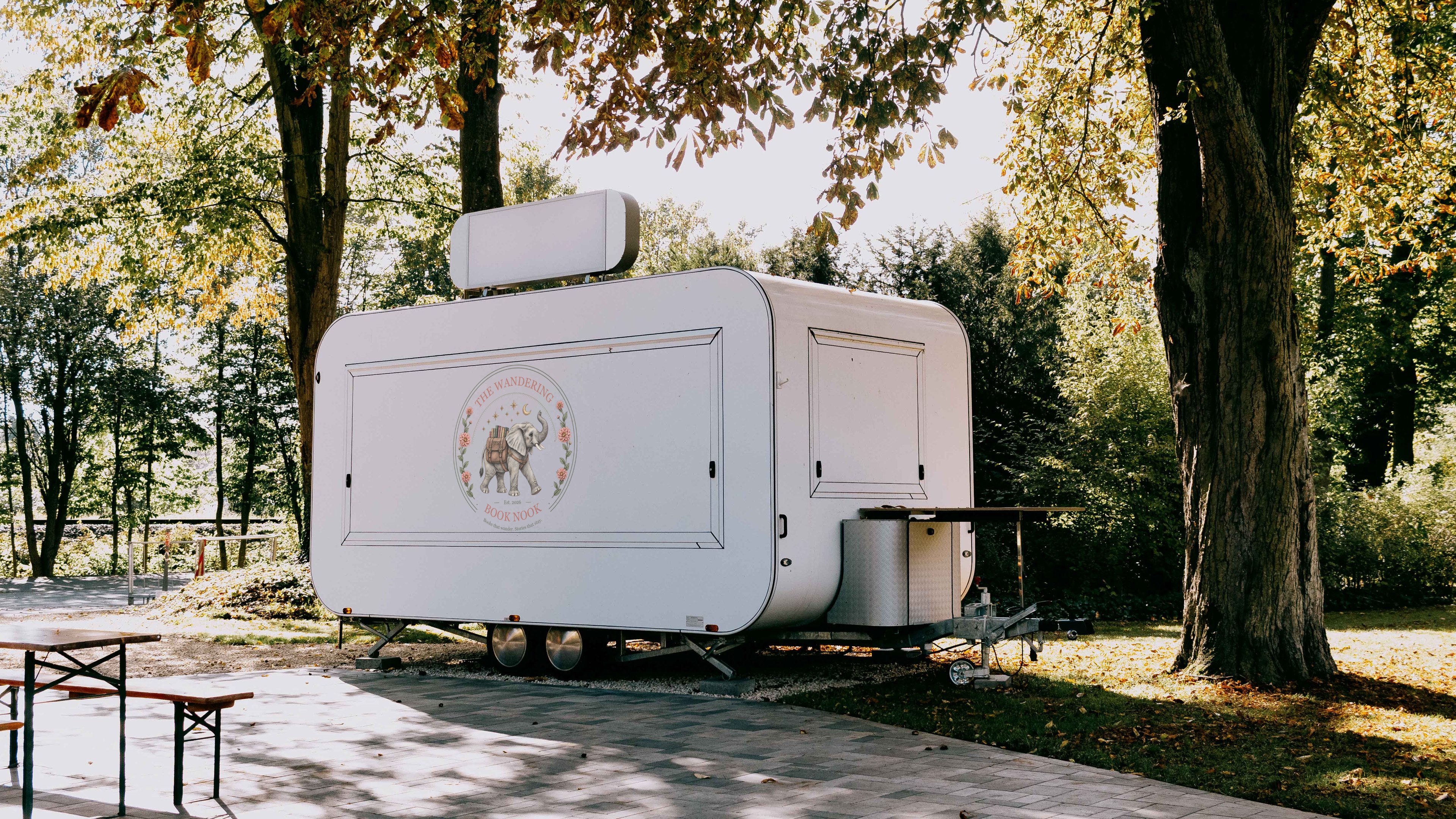 White book trailer under autumn trees with The Wandering Book Nook elephant badge on its side