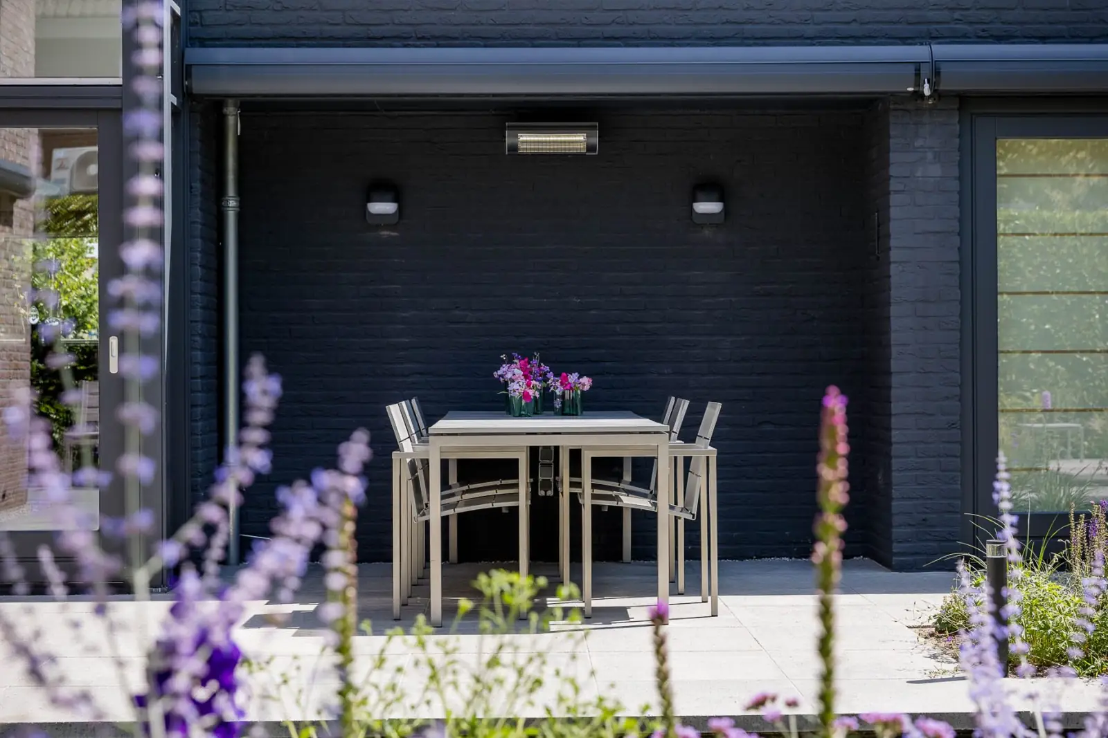 Eettafel onder de overkapping met terrasverwarmer en wandlampen in Almelo