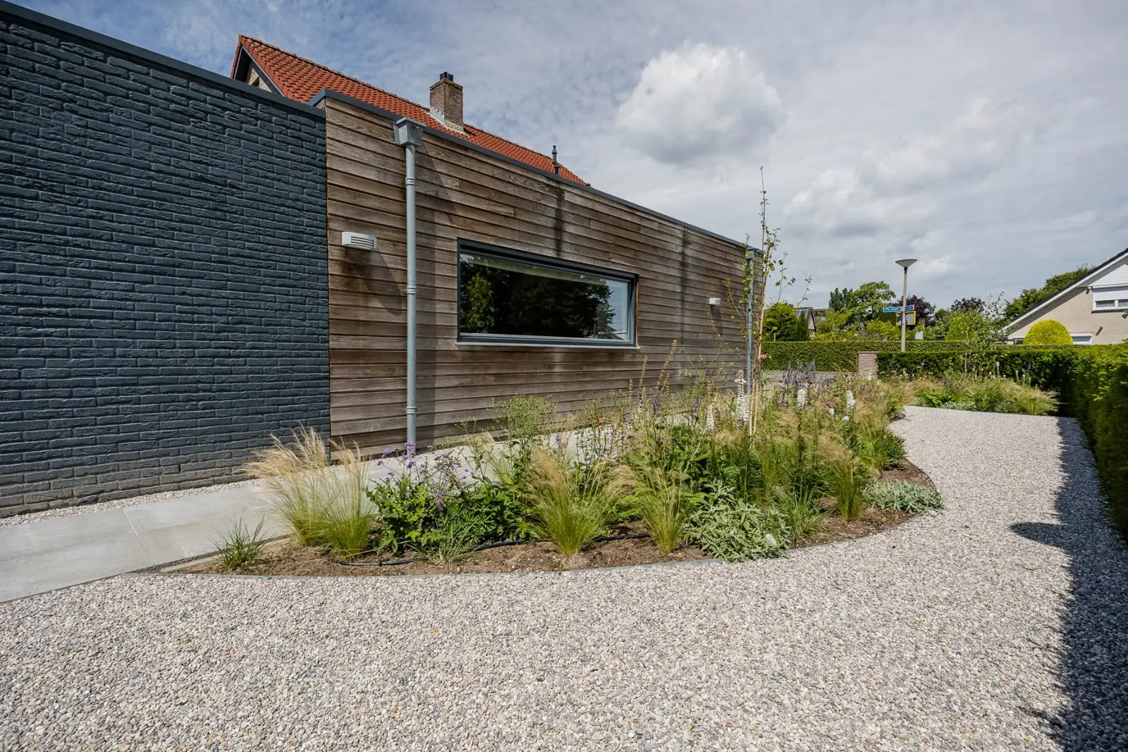 Houten gevel met grind en een prairieborder met vedergras in de voortuin in Almelo