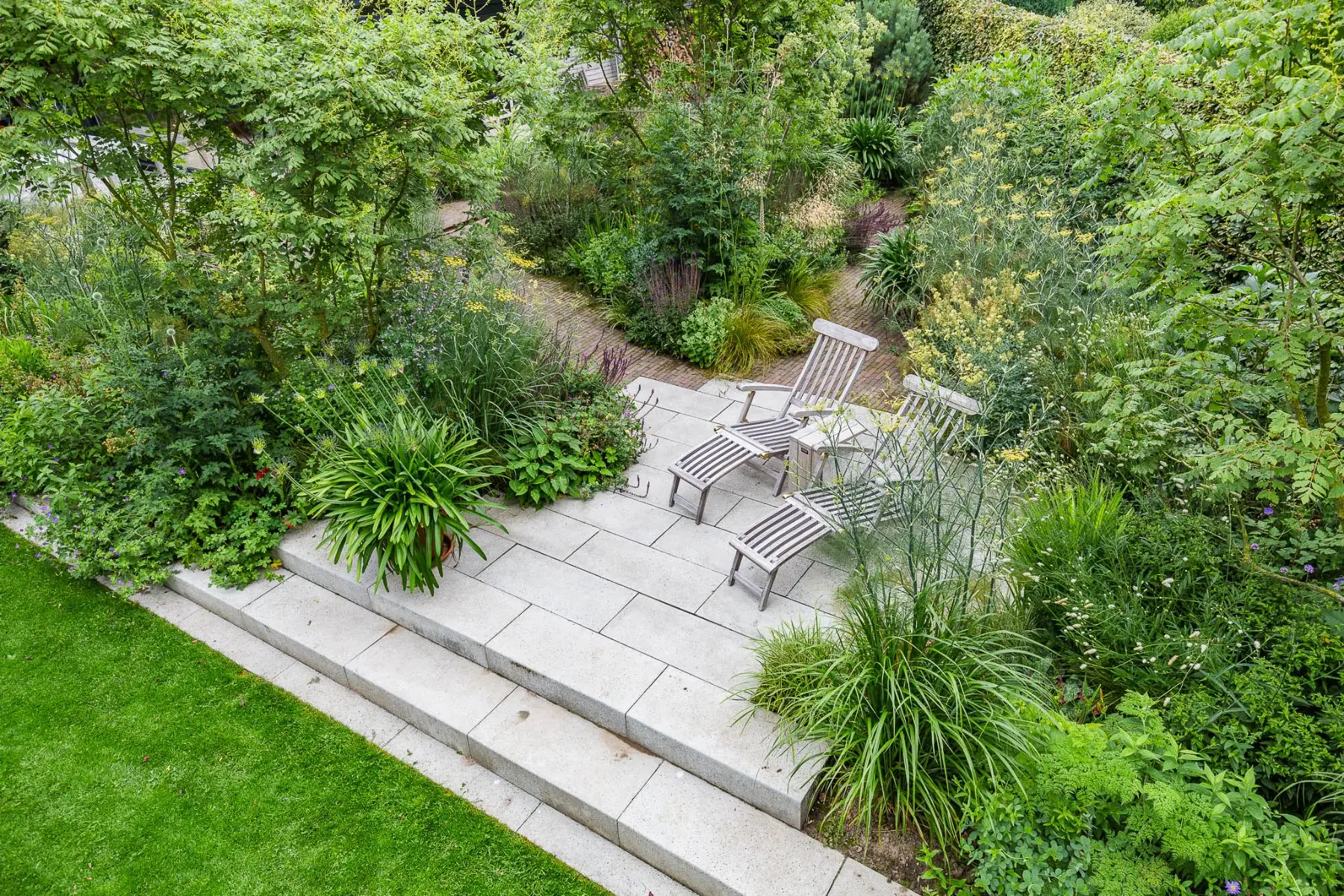 Tuin in Twello met natuurstenen terras, brede trap naar het gazon en weelderige borders rond de woning
