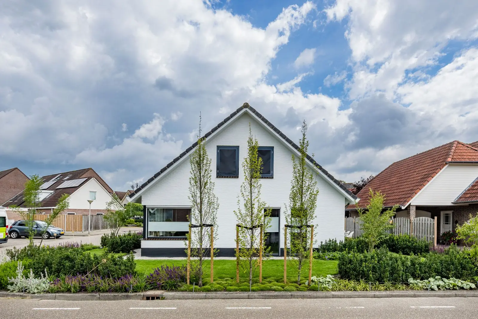 Hoekwoning met een voortuin van gazon, zuilbomen en brede borders langs de straat