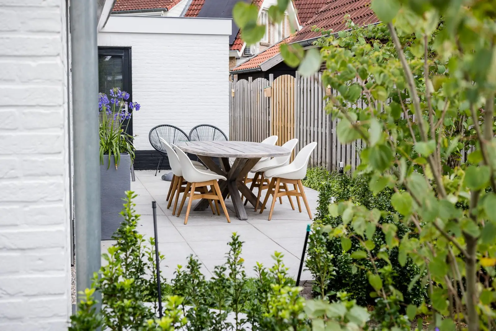 Terras met ronde eettafel en witte stoelen met doorkijk naar de schutting