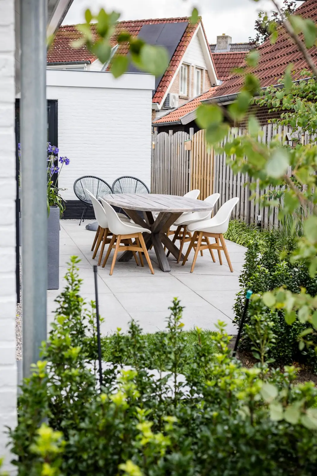 Terras met eettafel aan de witte gevel, gezien tussen de heesters door