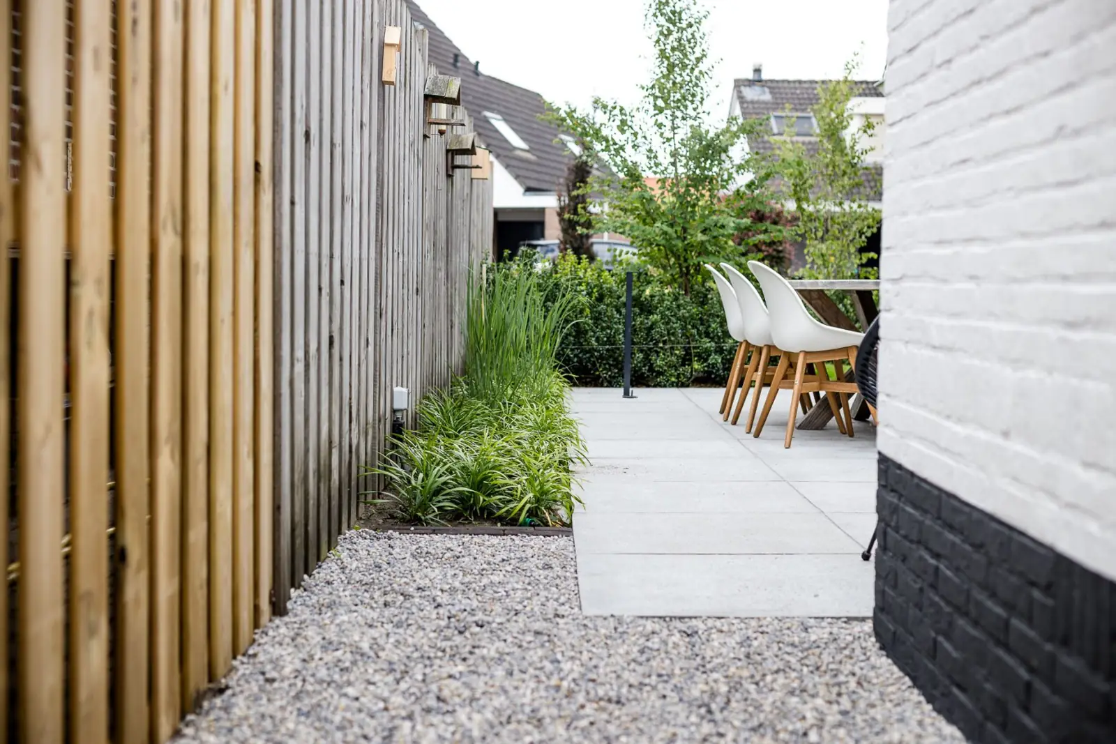Zijpad van grind langs een border met siergras naar het terras met eettafel