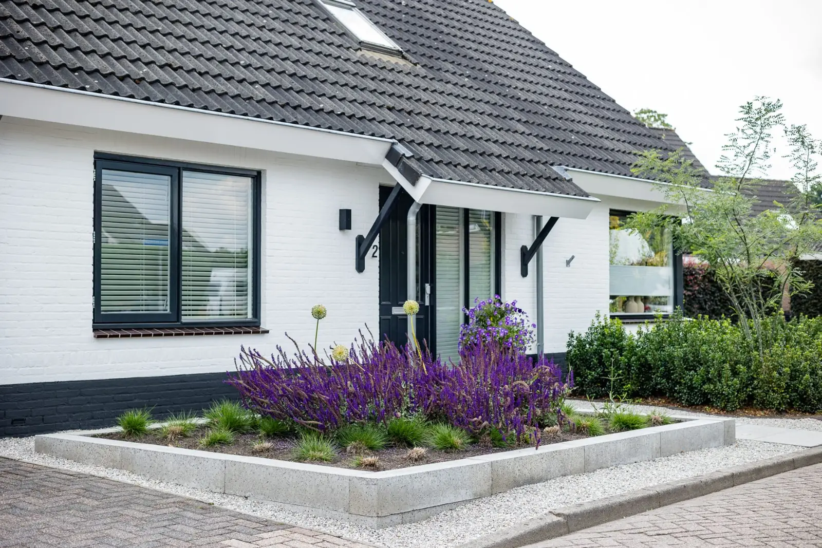 Witte woning met een verhoogd plantvak vol salie en sierui in de voortuin