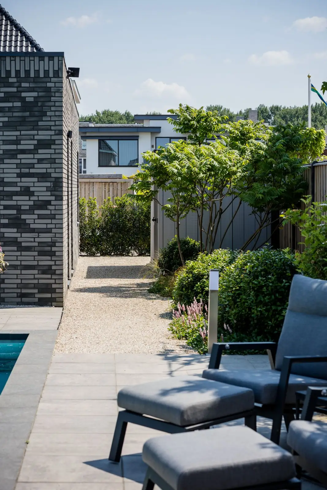 Zijpad van grind met sumak en een tuinlamp naast het zwembad in Almere