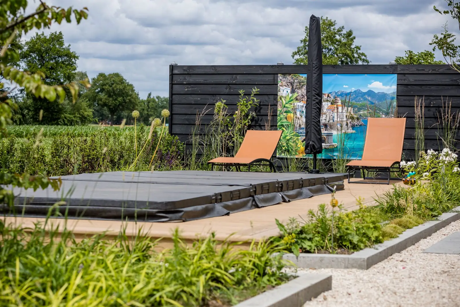Jacuzzi en ligbedden voor een zwarte houten schutting in een wellnesstuin in Hardenberg