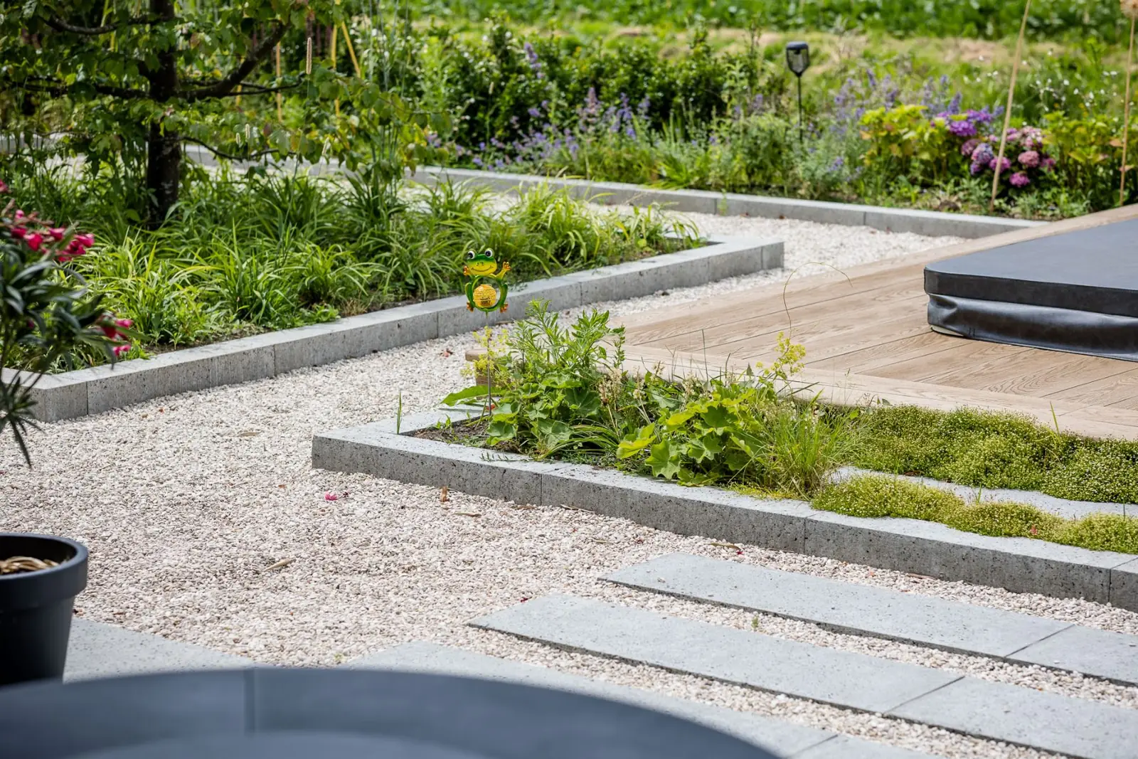 Grindpaden met betonnen opsluitbanden tussen borders en de jacuzzivlonder in Hardenberg
