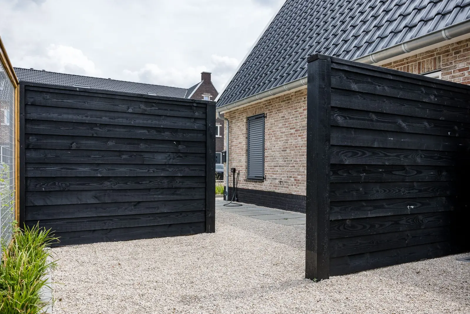 Zwarte houten schermen bij de oprit van grind aan de woning in Hardenberg