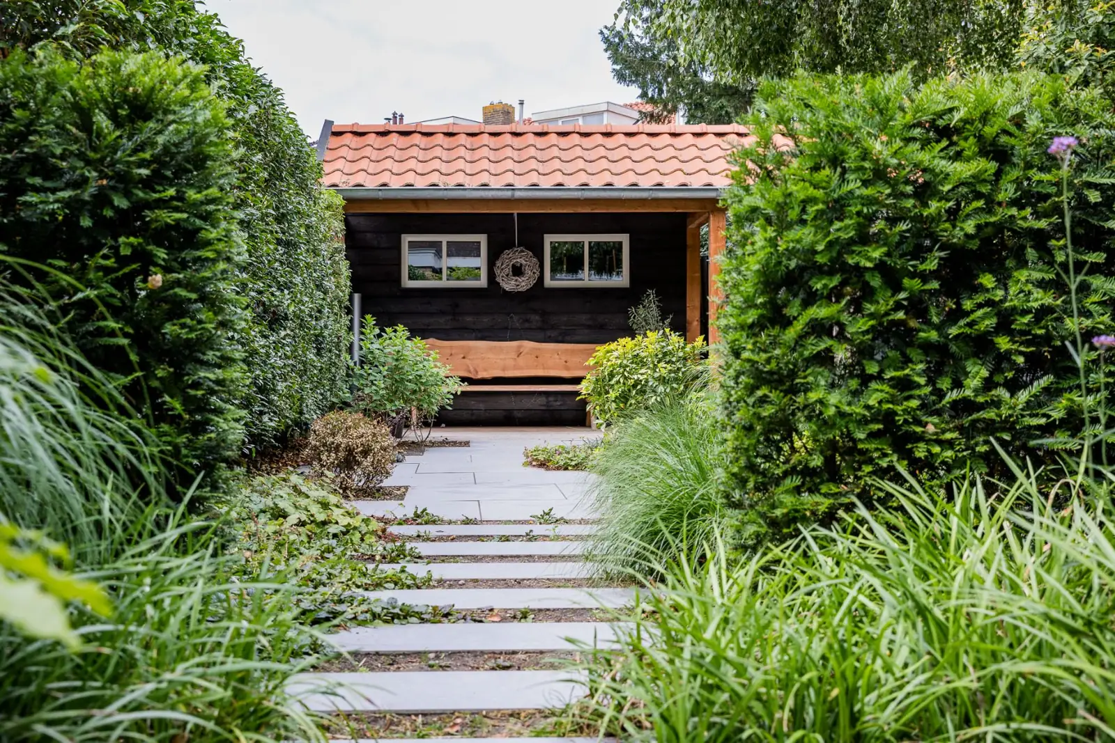 Keramische stapstroken als pad tussen taxus en siergrassen naar de overkapping in Zwolle