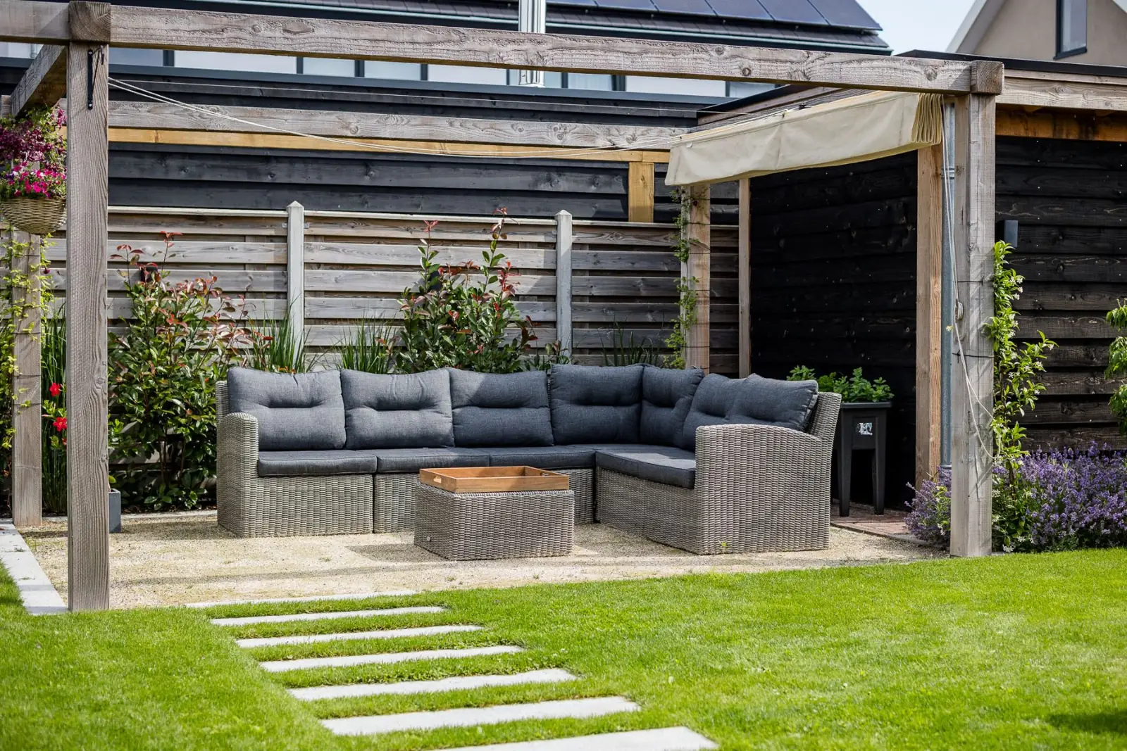 Loungeplek onder een houten pergola met harmonicadoek in een strakke tuin in Lemelerveld