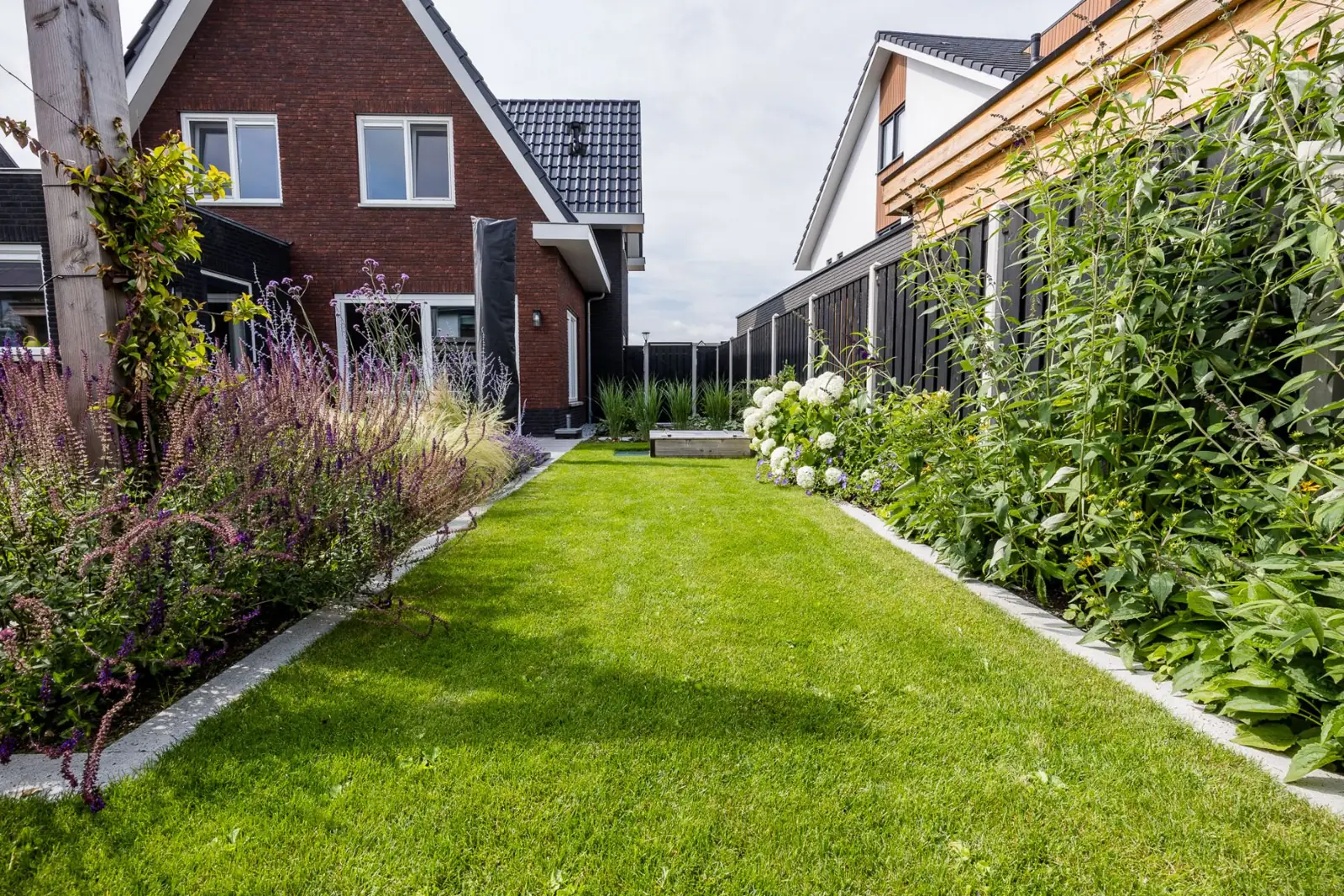 Gazon met strakke betonranden en borders richting de woning in Lemelerveld
