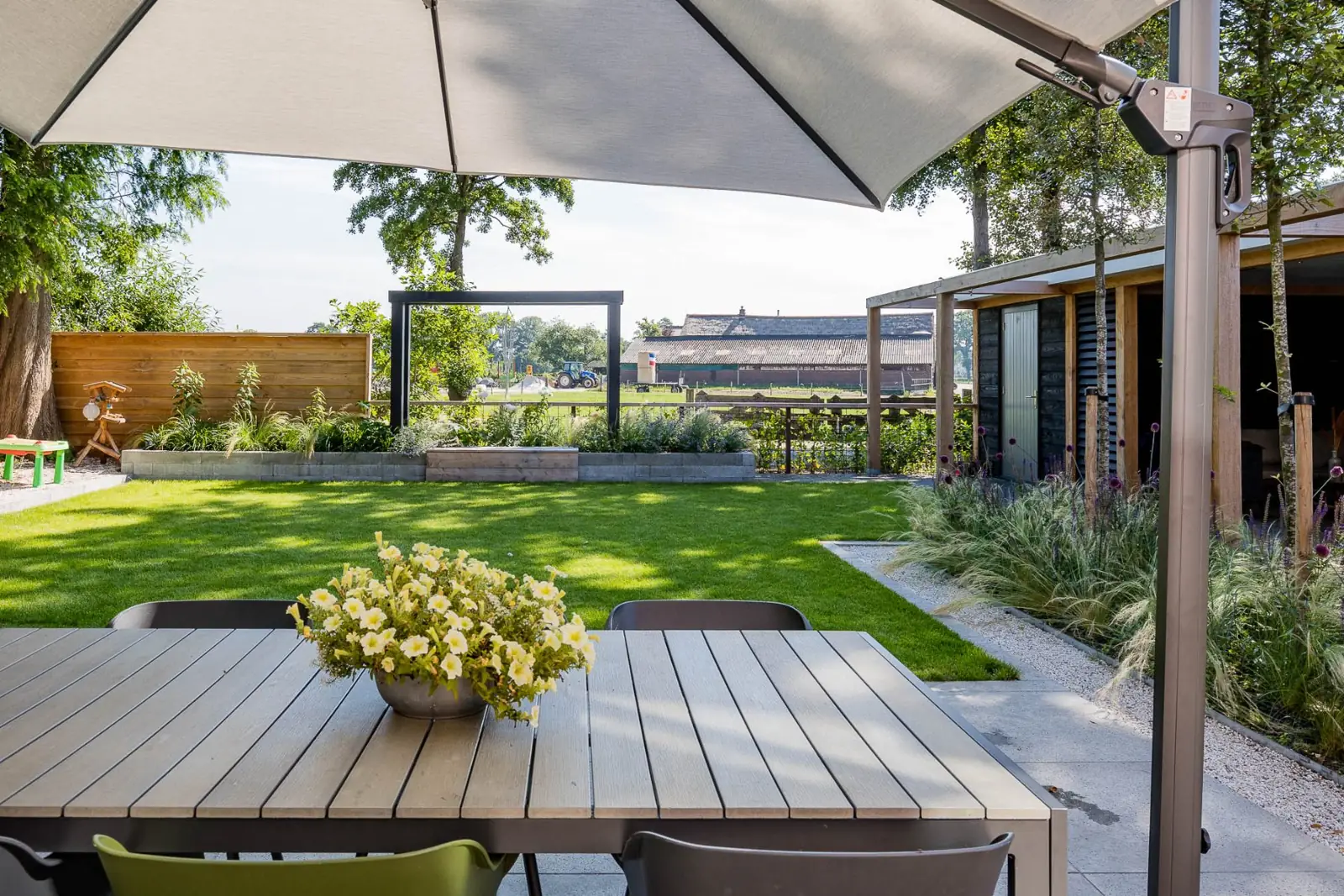 Terras met eettafel onder een parasol en uitzicht over het gazon naar het weiland in Hardenberg
