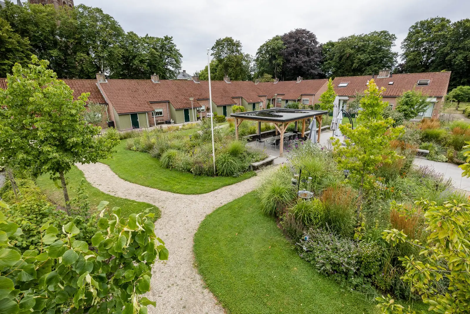 Binnentuin in Raalte met kronkelende grindpaden, gazon en een houten overkapping tussen de seniorenwoningen