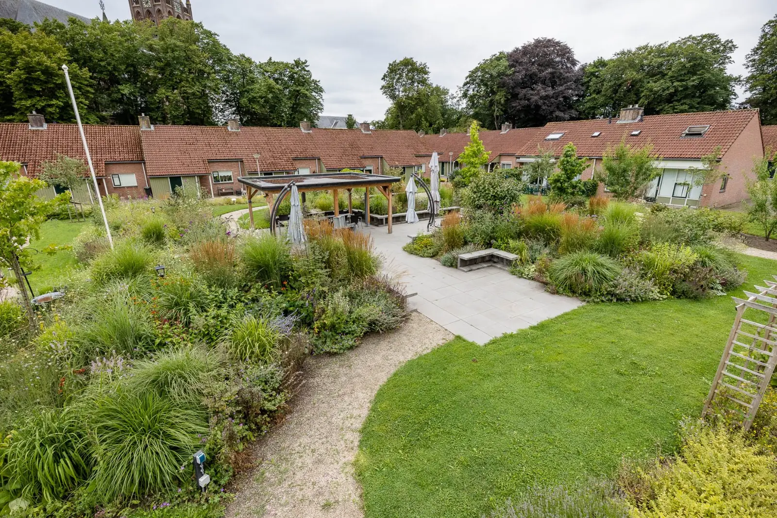 Terras met zitmuren en overkapping tussen borders vol siergrassen en vaste planten in Raalte