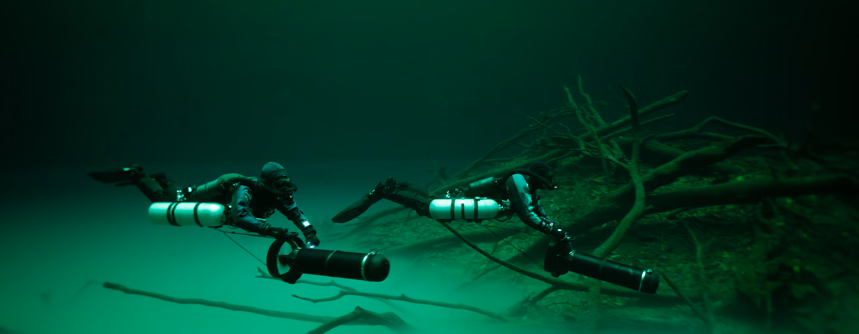 2 divers propelling across the ocean bottom next to driftwood