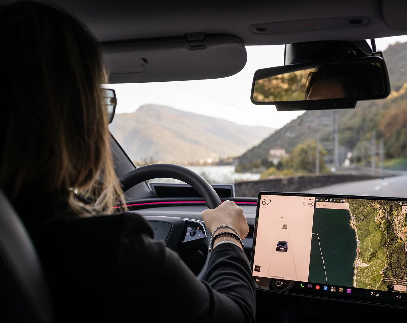 Autista donna al volante della Tesla taxi con paesaggio ticinese sullo sfondo