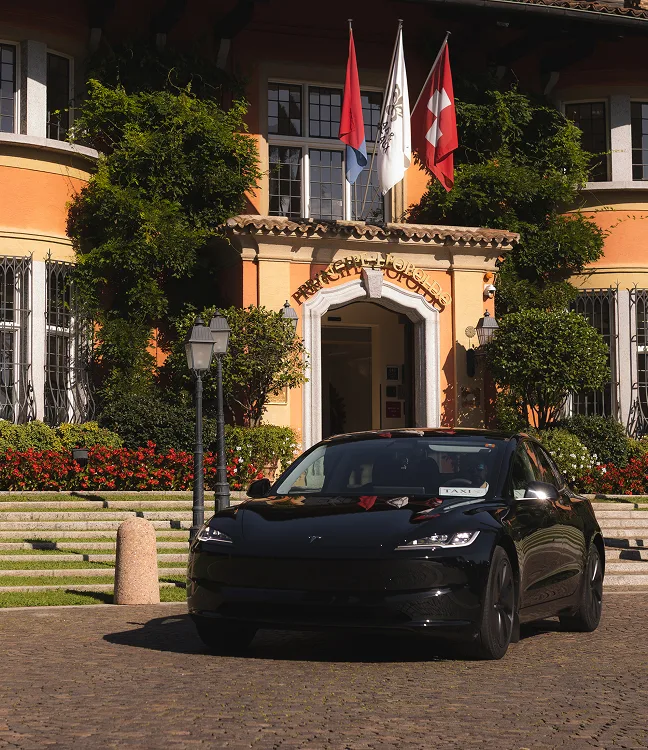 Taxi Tesla Model 3 nera davanti a hotel di lusso in Ticino