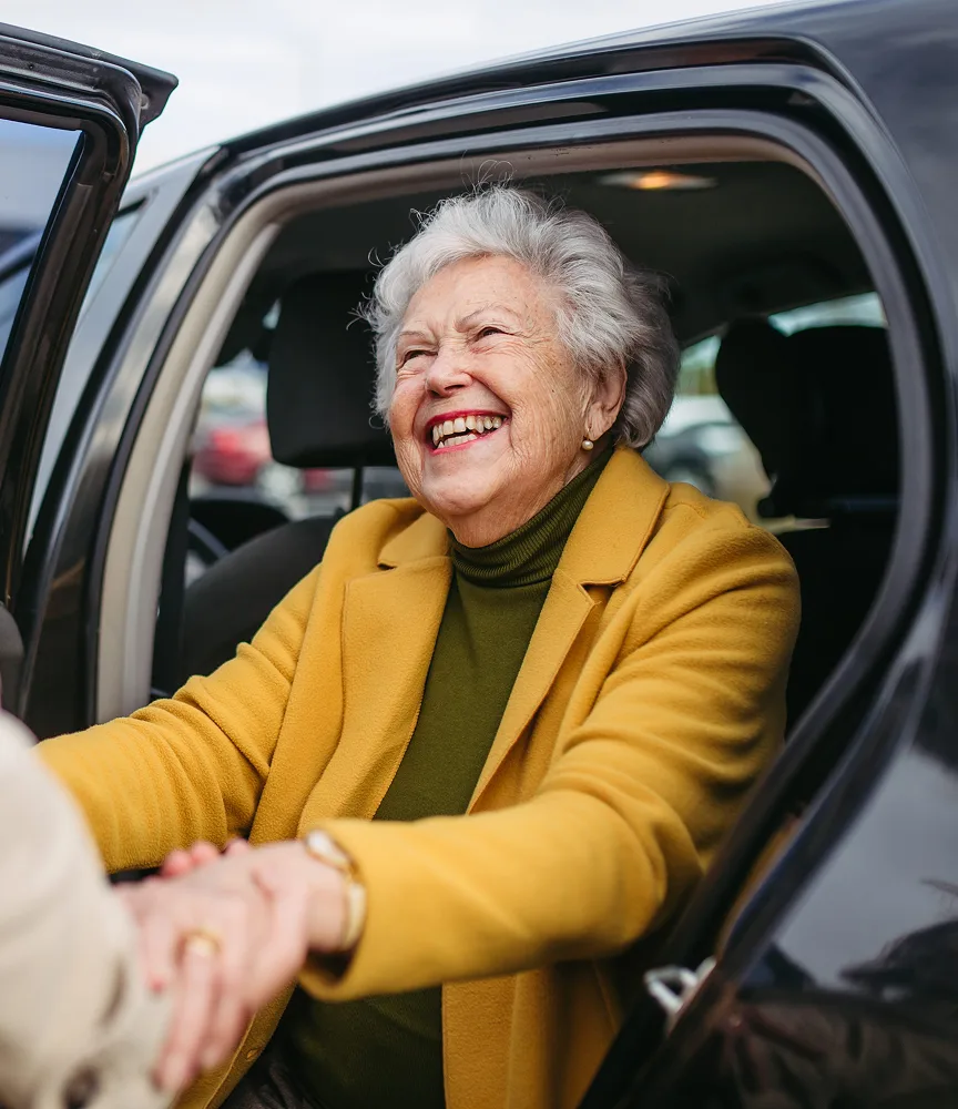 una mano che aiuta una signora anziana a salire su un'auto nera, senza il volto dell'autista