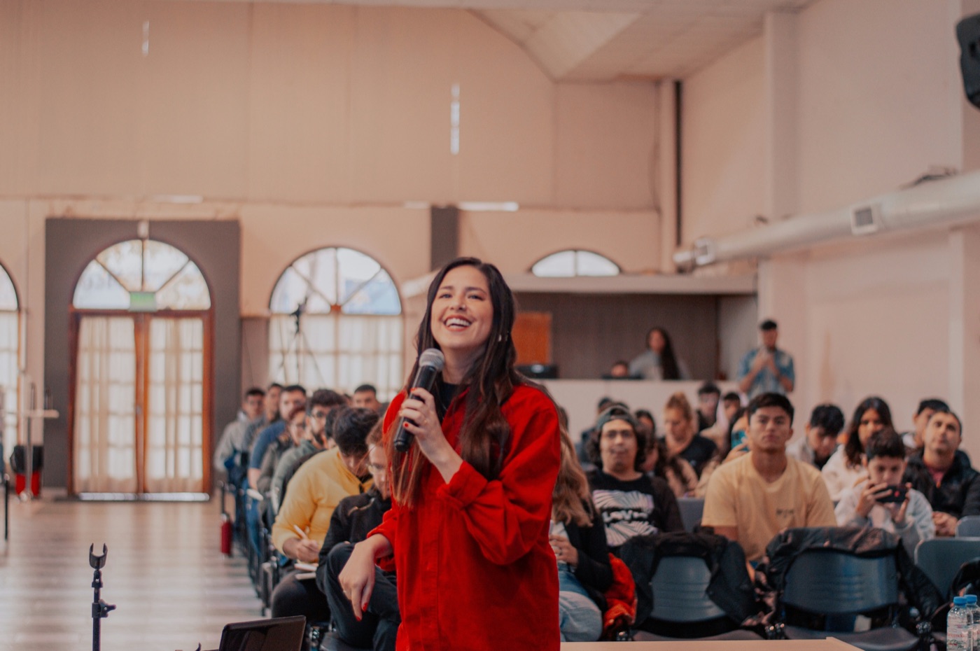 A young woman speaking to a room full of young people.
