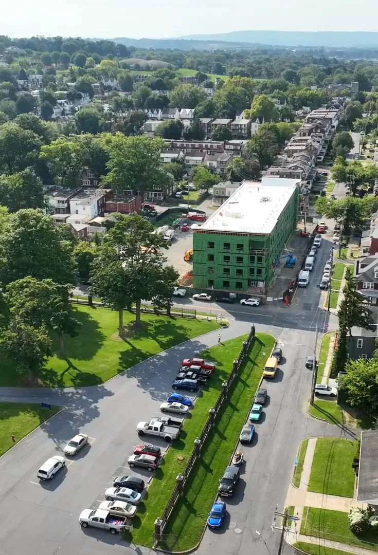 Aerial view across the neighborhood: the red-brick armory and its lawn in front, Woodward Lofts with its white roof farther up the tree-lined street.