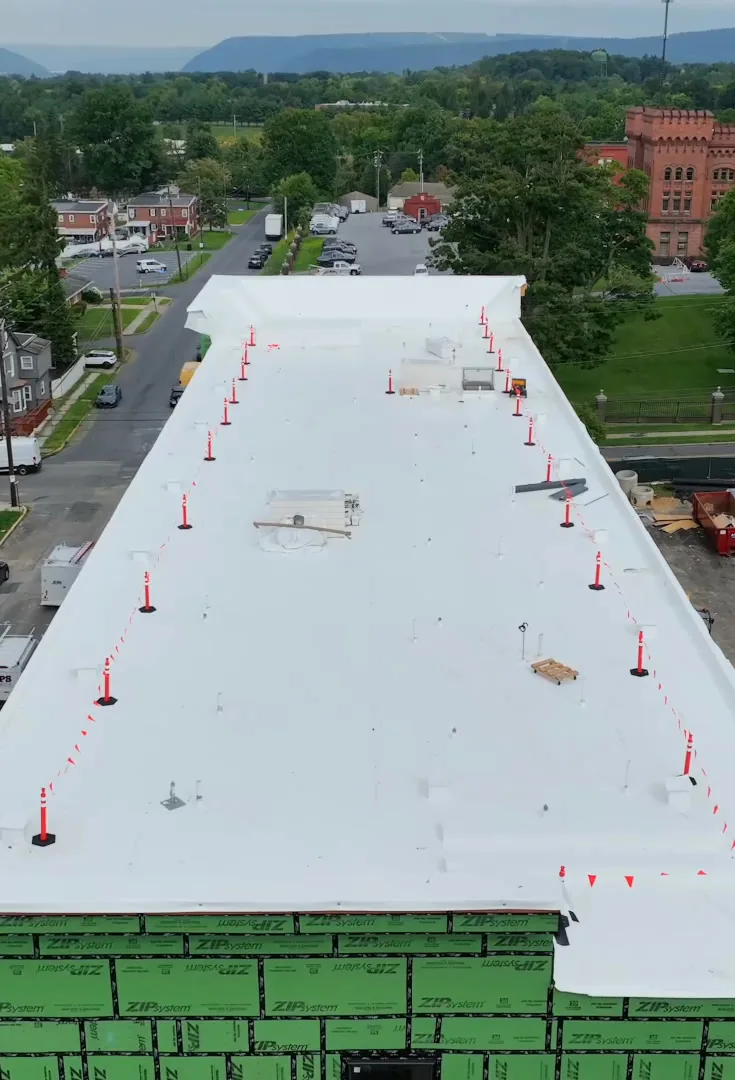 Aerial view of the new white roof with orange safety markers, the brick armory and the Allison Hill streets beyond.