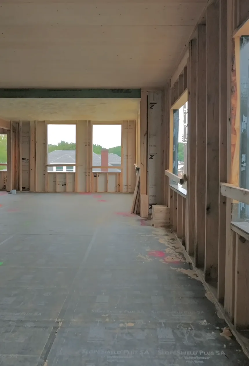 A top-floor room with a timber ceiling and stud walls, open to a view of neighboring houses.