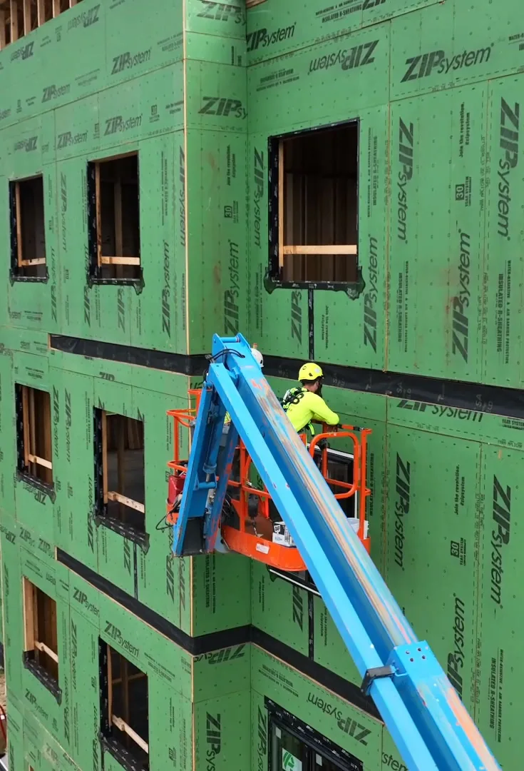 A worker in a lift at the corner of the building, with a parking lot and lawn below.