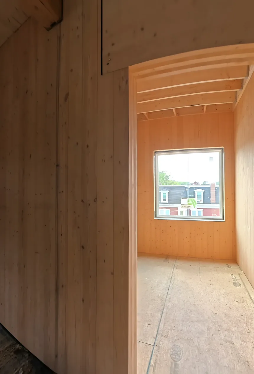 An unfinished timber room with a doorway into a smaller room with a window.