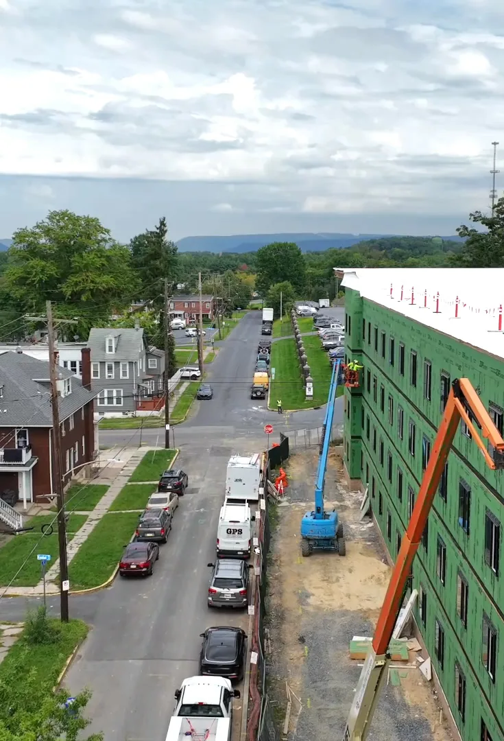 Aerial view along the street beside the building, with lifts at the facade and houses across the street.