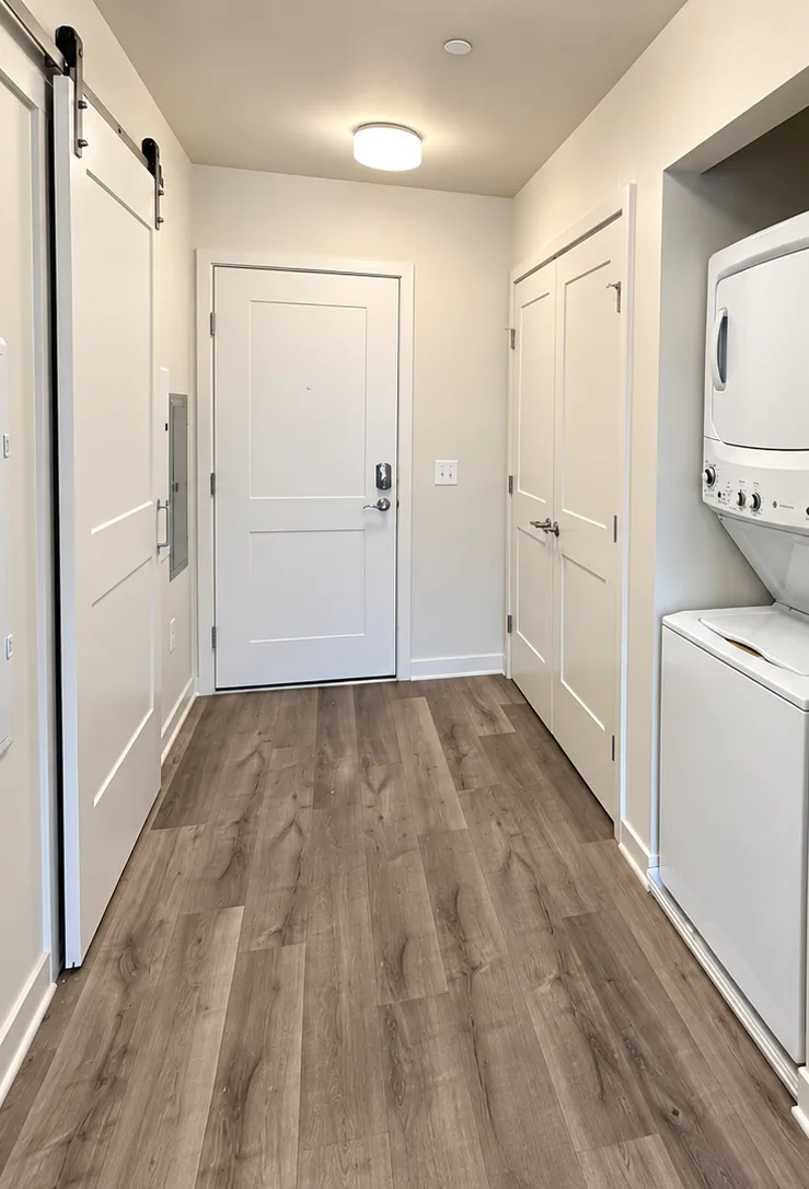 The entry hall of a studio, with a sliding barn door, a stacked washer and dryer and the front door.