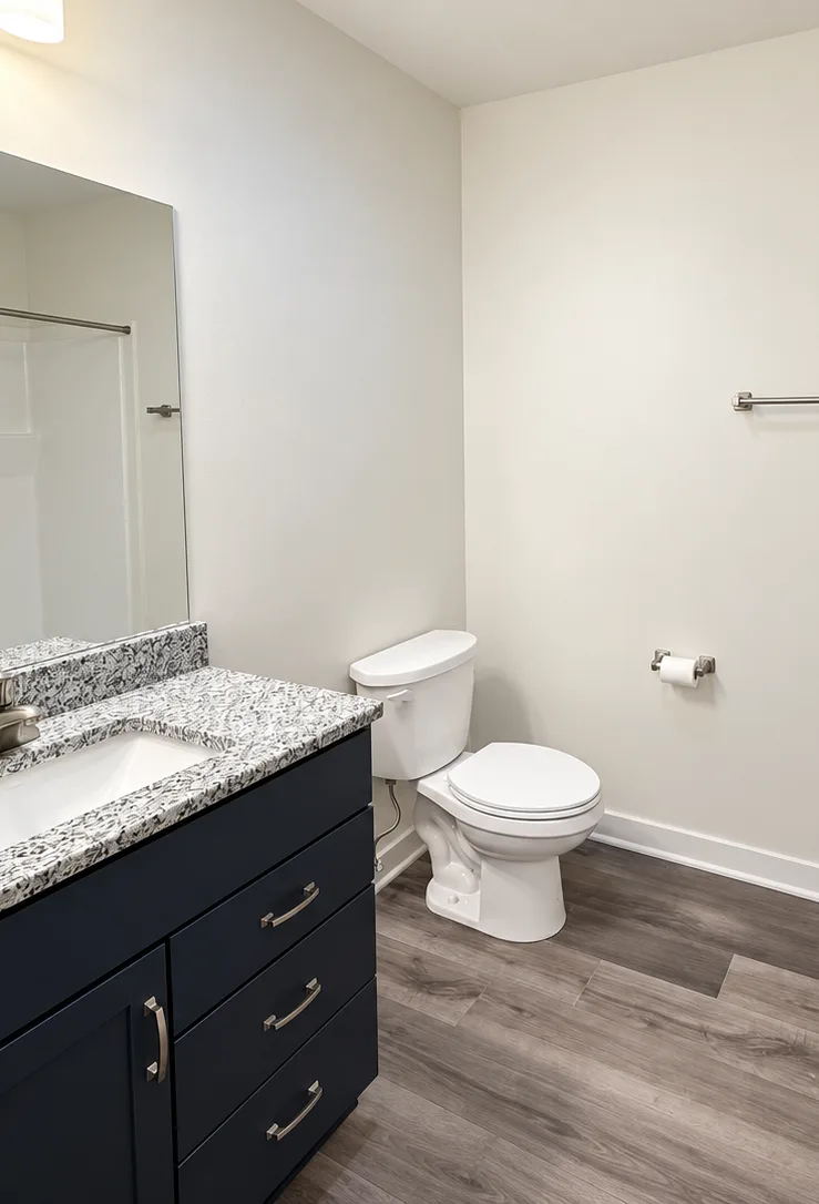 A Sycamore Homes studio bathroom with a navy vanity, a speckled countertop, a toilet and a walk-in shower.