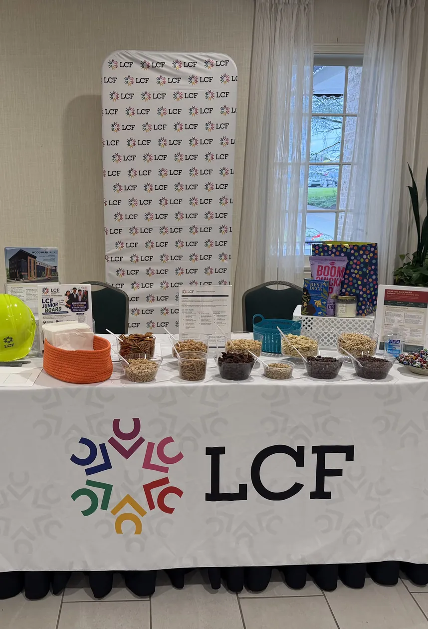 An LCF information table with snacks, a yellow hard hat and flyers, in front of an LCF banner.