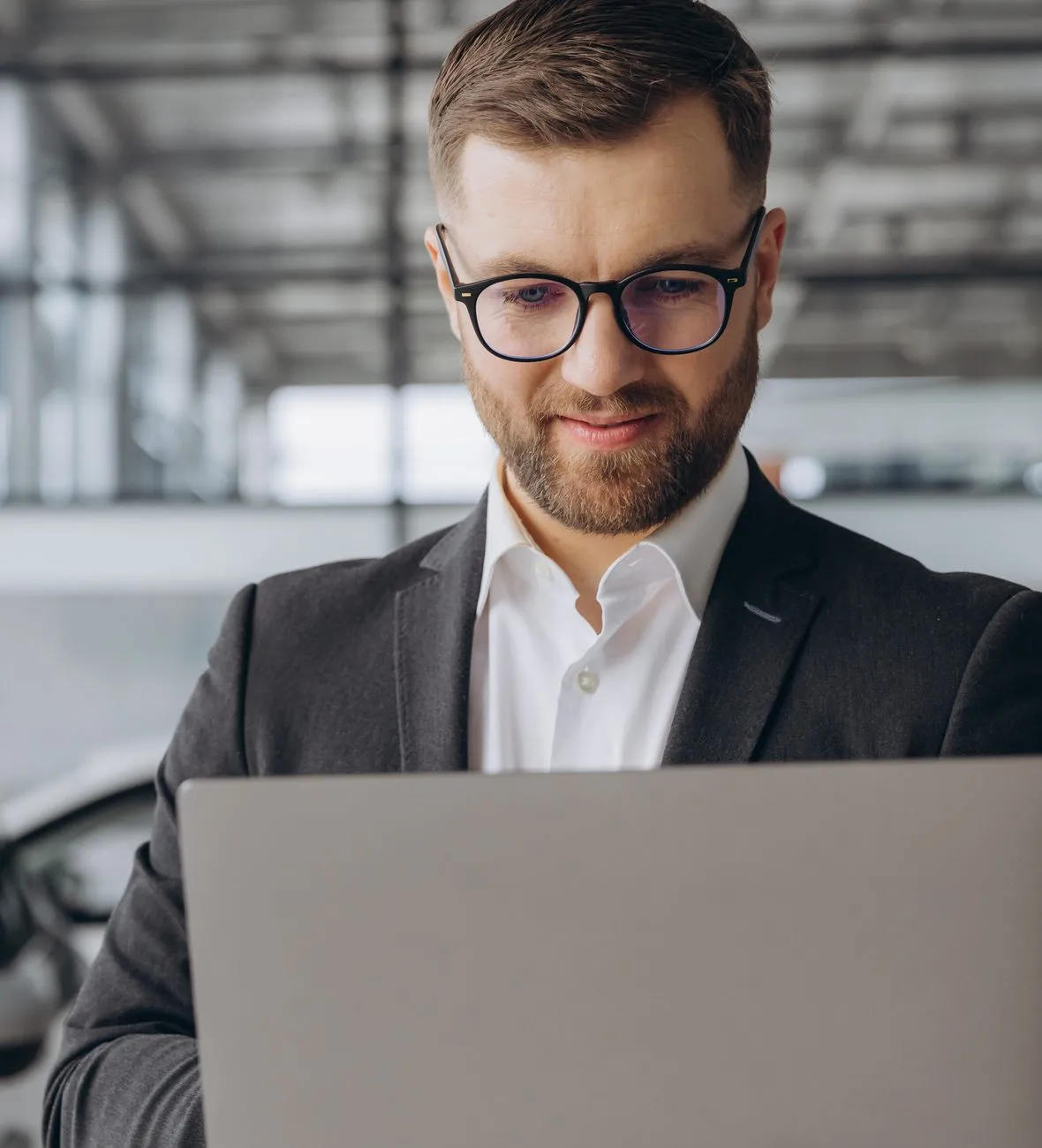 Car sales consultant in glasses using a laptop inside a dealership
