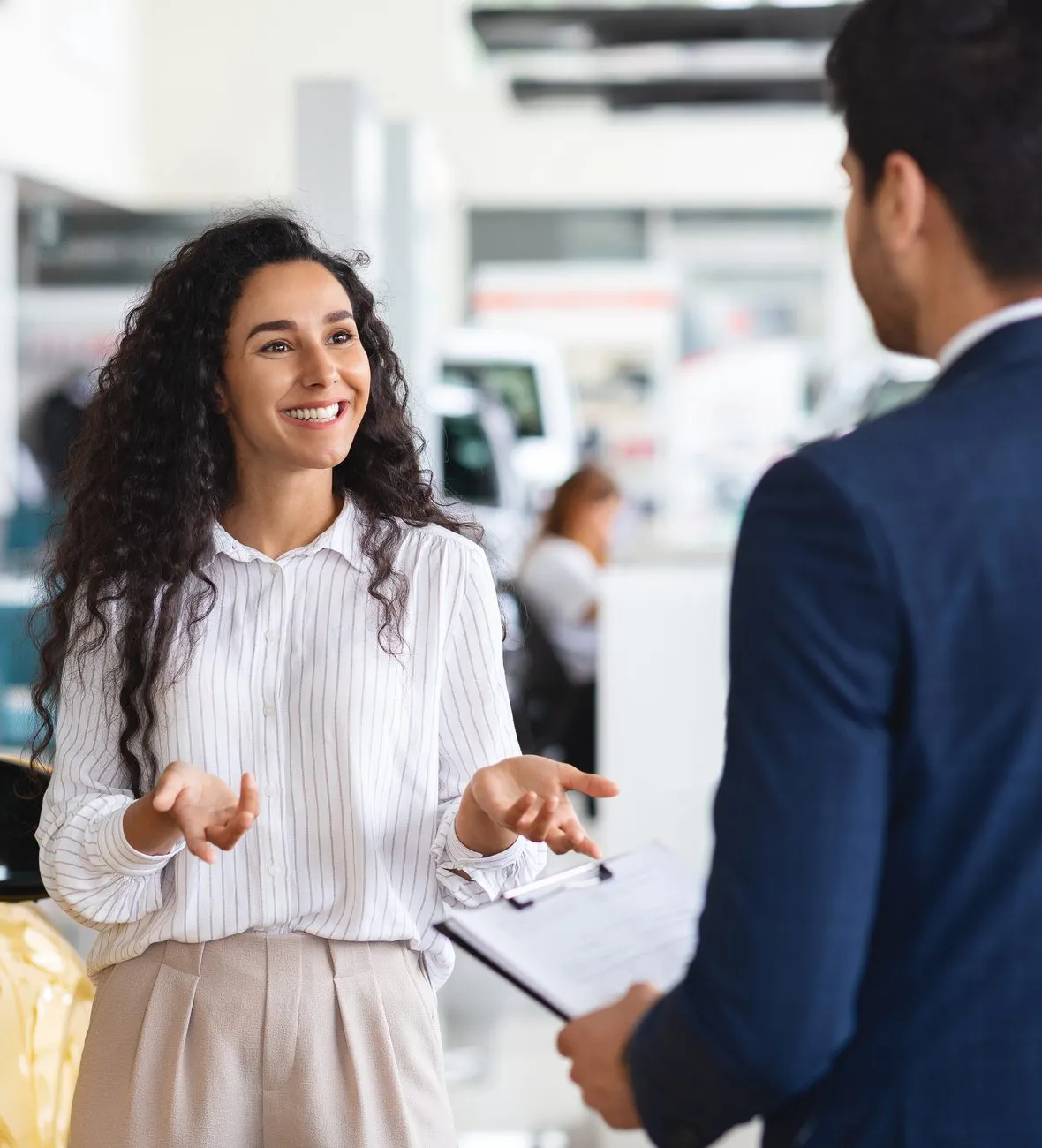 Smiling woman talking with a sales associate at a car dealership