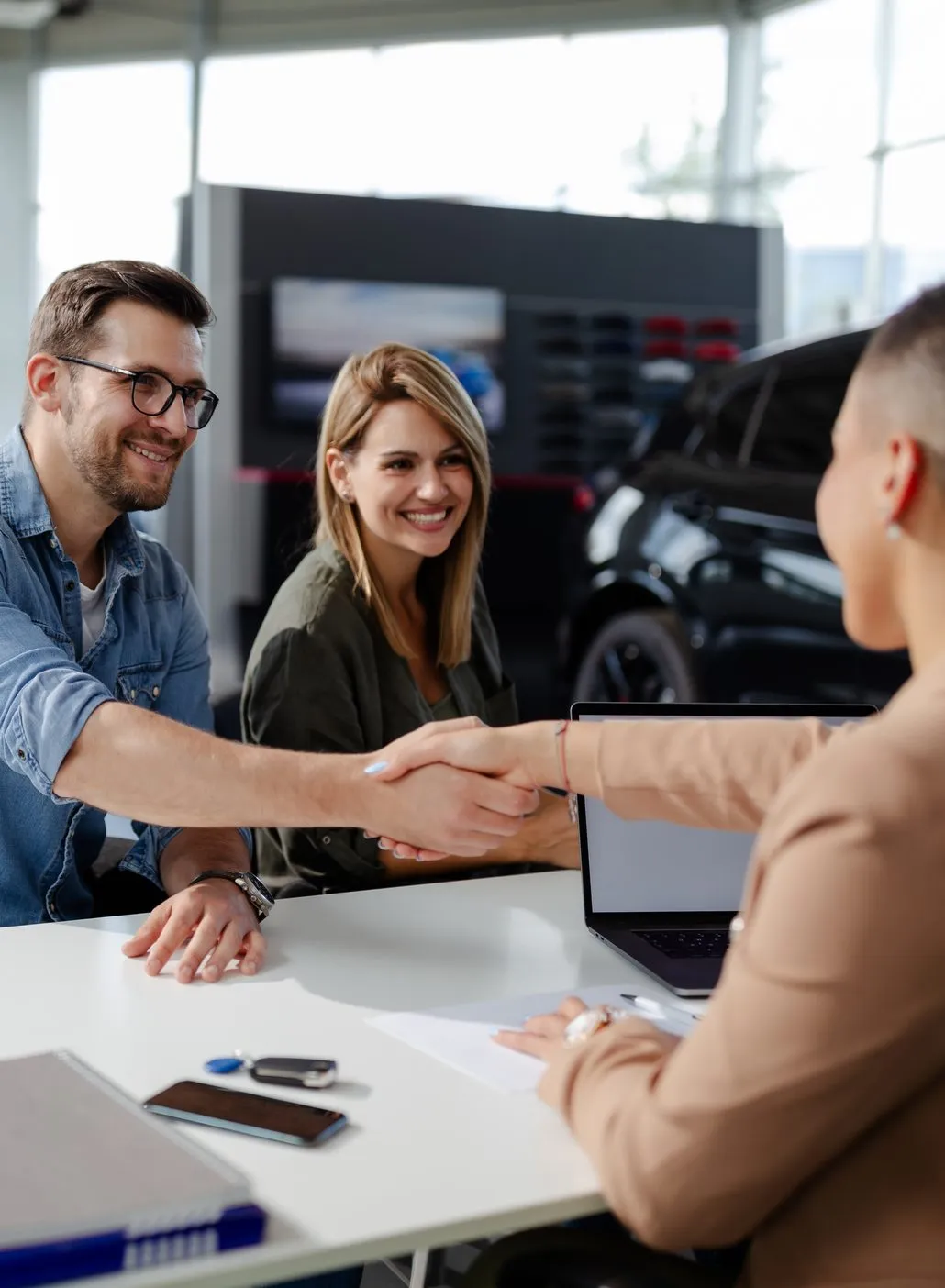 Customer shaking hands with a dealer across a desk in a car showroom