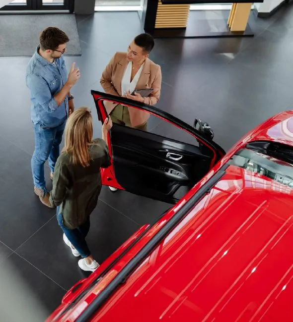 Overhead view of a couple looking at a red car in a dealership showroom