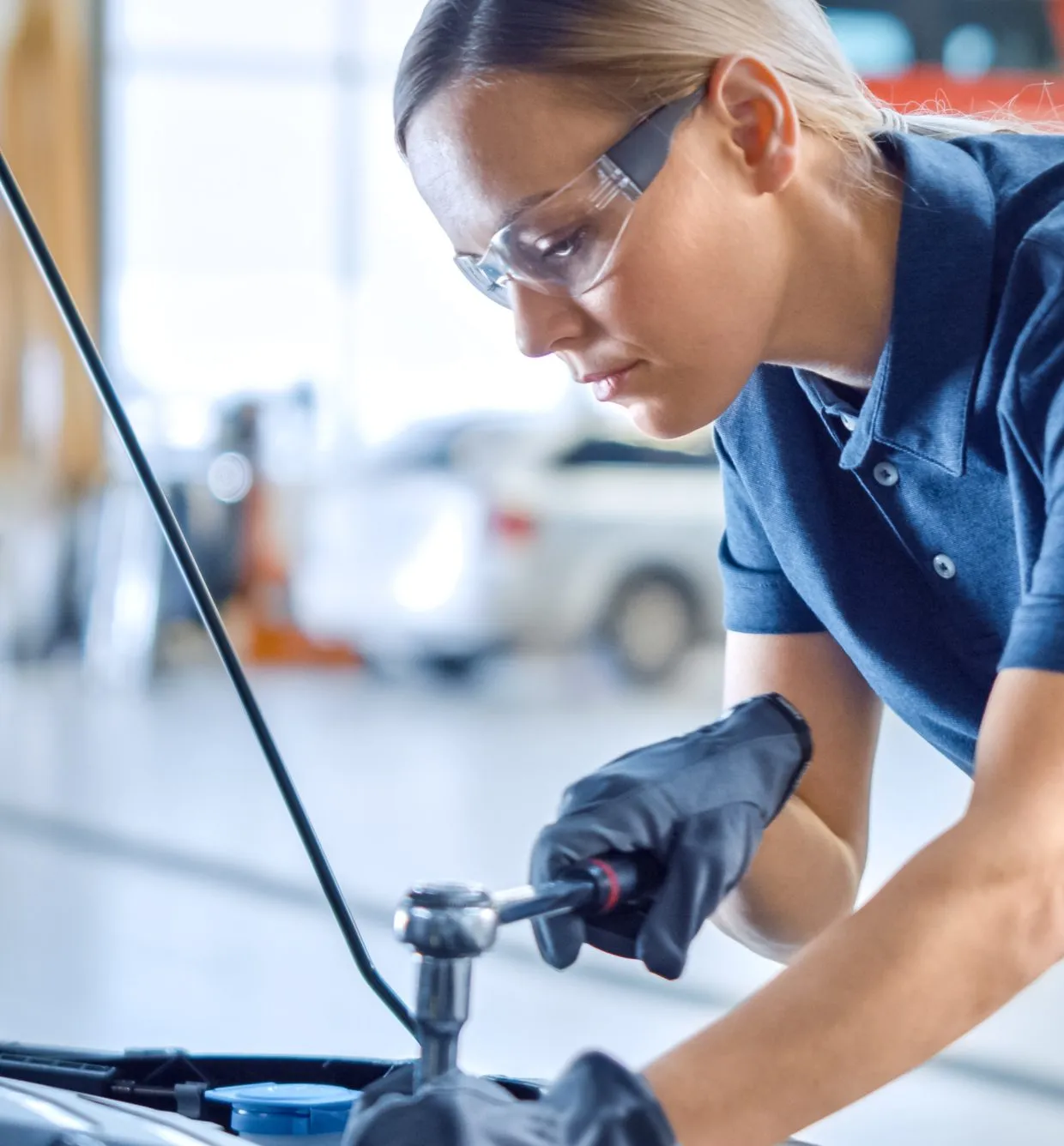 Service technician working under the hood of a car in a dealership service bay