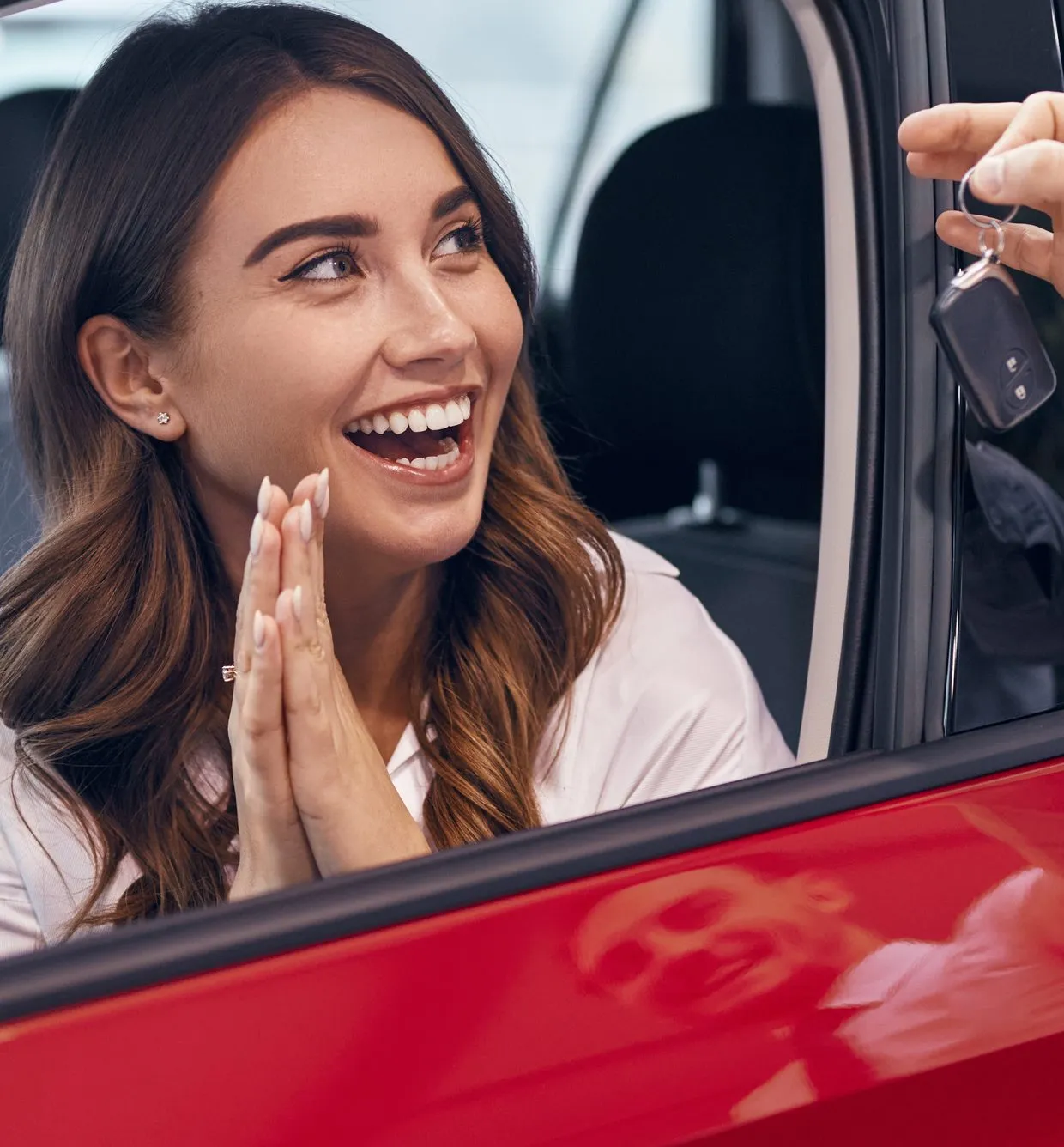 Excited woman in a red car receiving the keys to her new vehicle