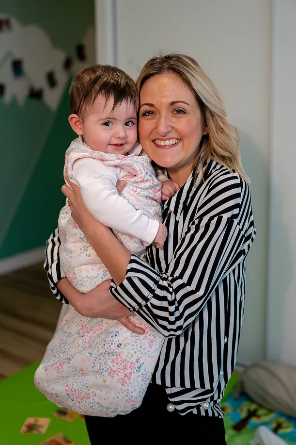 Une adulte souriante porte un bébé dans une micro-crèche Minimoy