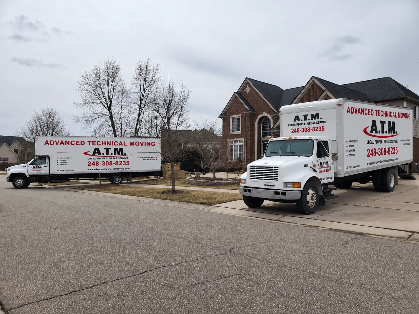 Two Advanced Technical Moving trucks parked at a brick home in a residential neighborhood