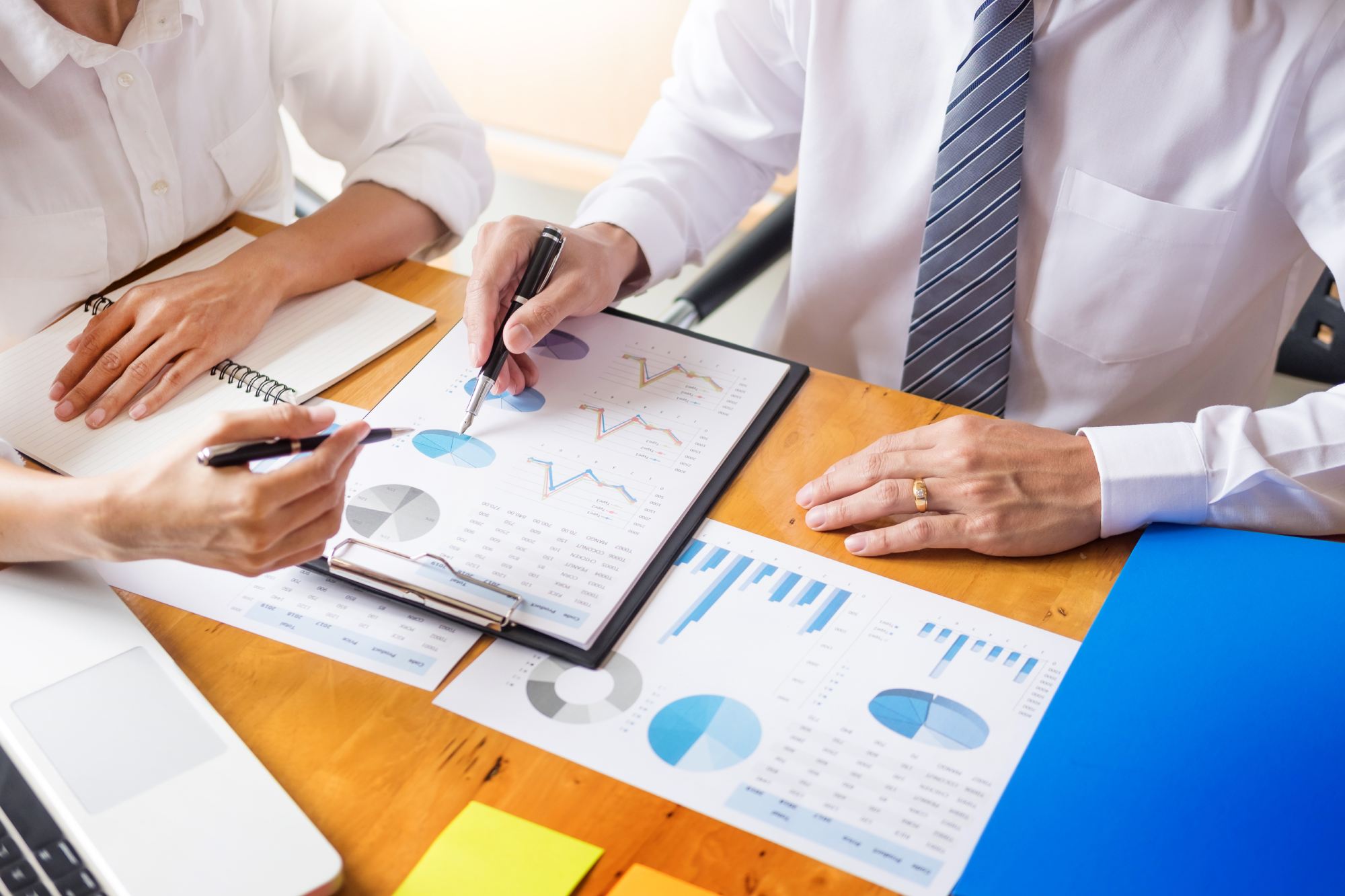 Two business professionals reviewing charts and graphs on printed reports at a wooden desk.