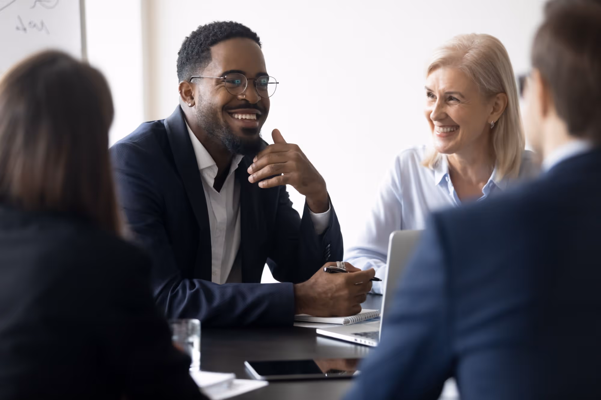 Smiling diverse businesspeople having a meeting at a conference table with laptops and notebooks.