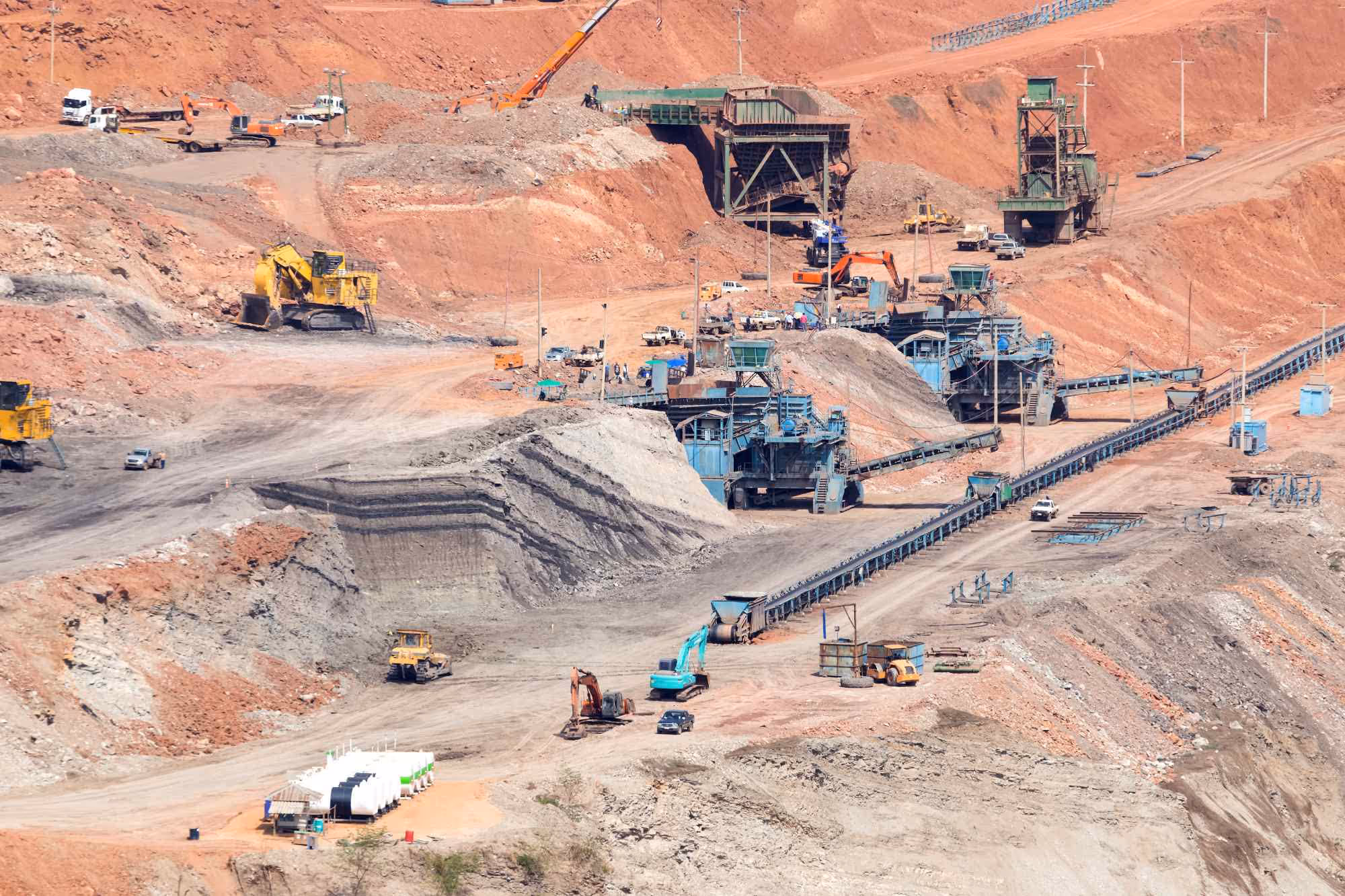 Open-pit mining site with heavy machinery, conveyor belts, and large piles of earth and rocks.