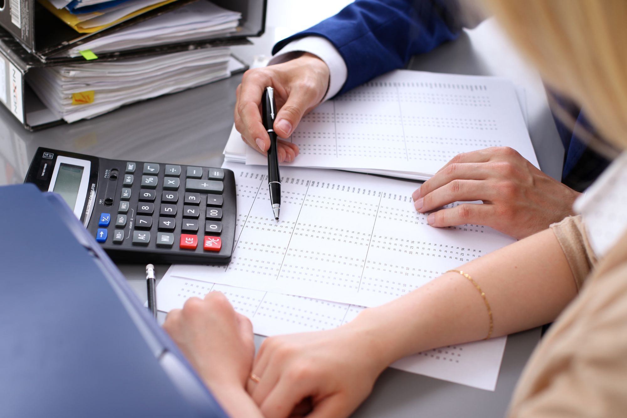 Two people reviewing financial documents with a calculator and pen on a desk.