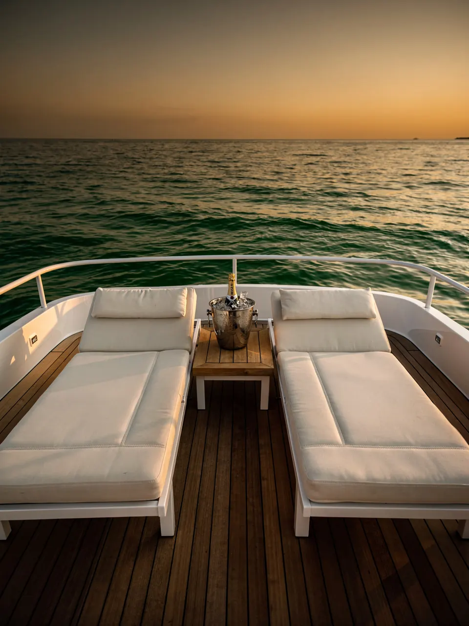 Two loungers on the teak deck of a yacht facing the sea at sunset